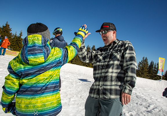 Shaun Cattanach, winner of PSIA-AASI's 2019 Distinguished Service Award, high-fives a child who learned to snowboard at Interski 2019 in Bulgaria.