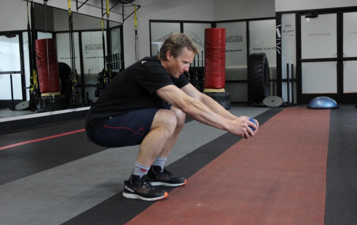 Man does a squat in gym while holding a medicine ball