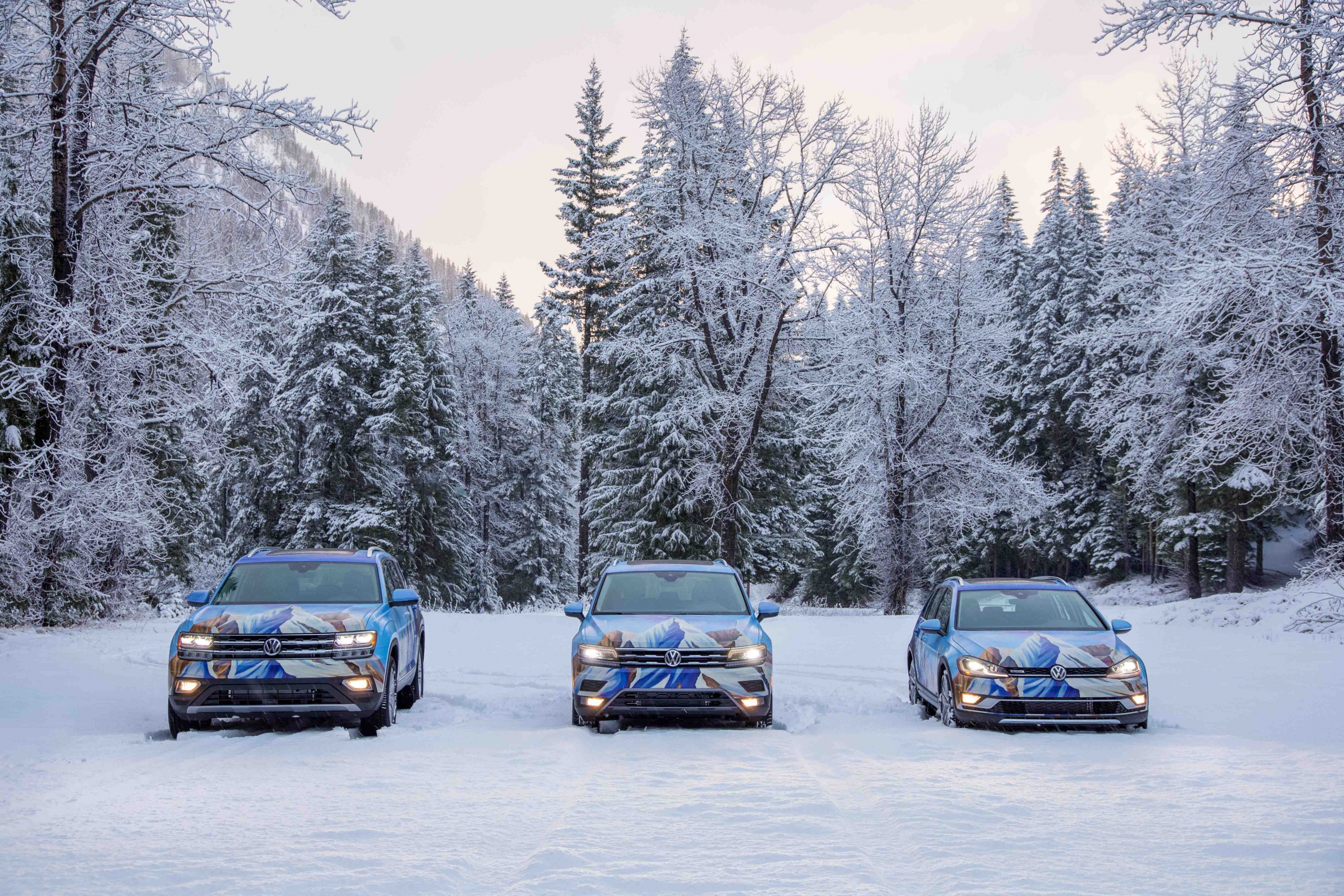 The PSIA-AASI custom painted Atlas Tiguan and Alltrack are parked in a snow covered parking area facing the camera