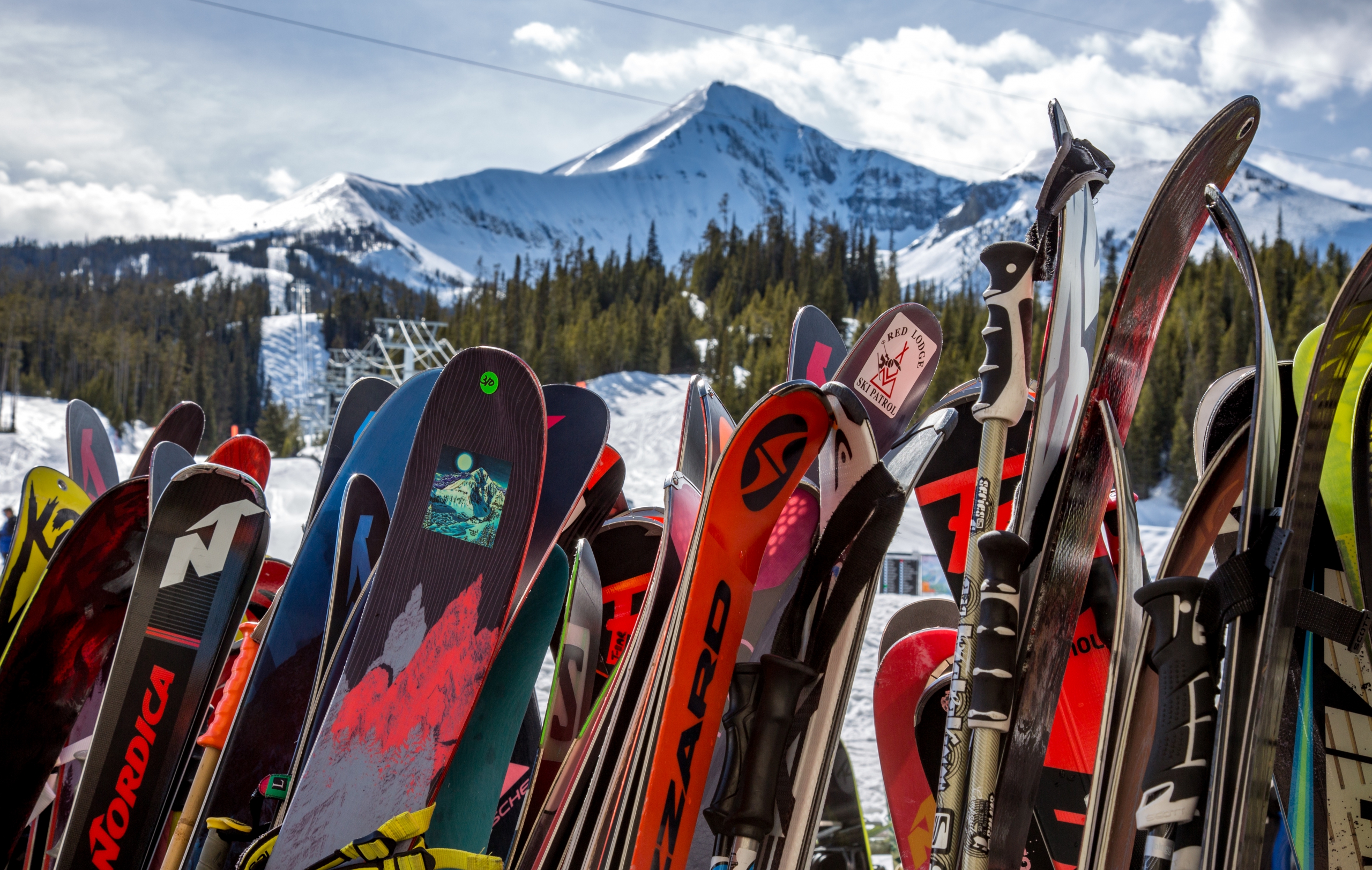 Skis and snowboards rest on a ski rack with Big Sky's Lone Peak in the background