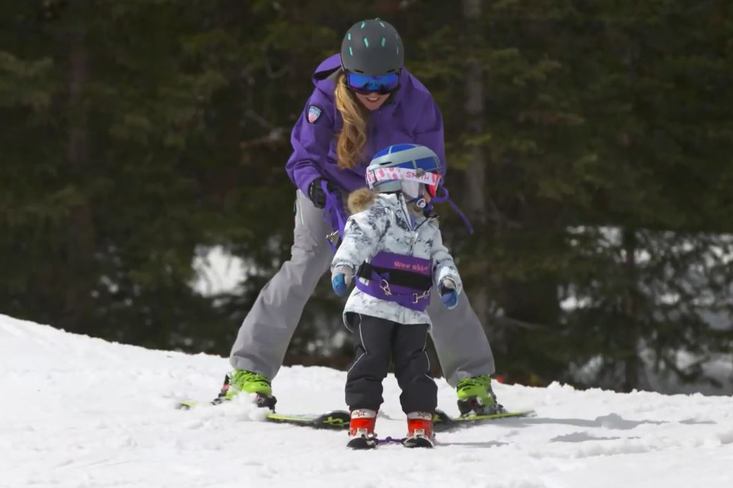 A mom teaches her daughter to ski using a hoop.