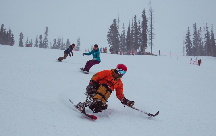 An adaptive skier descends a ski run ahead of two snowboarders