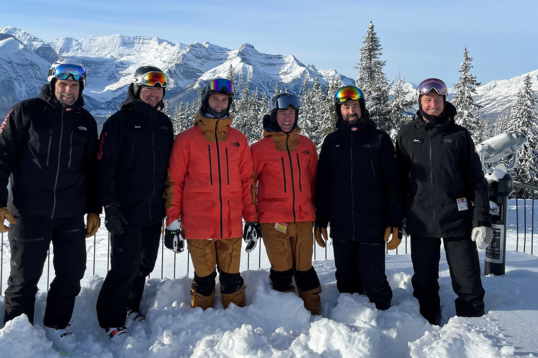 PSIA and CSIA instructors stand together at the top of a mountain