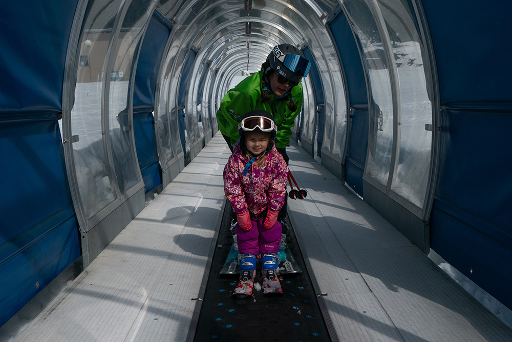 a ski instructor and their student ride the ski carpet