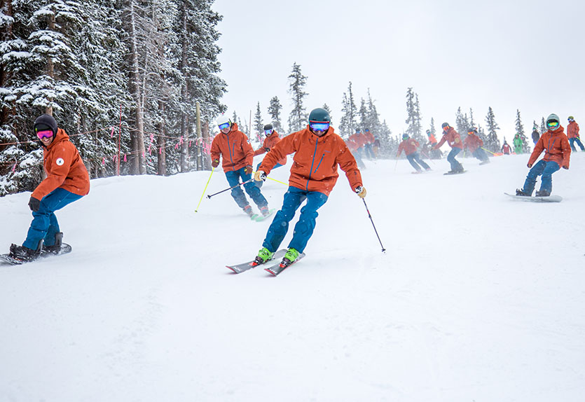 Alpine, snowboard, and telemark specialists on the PSIA-AASI National Team descend a slope together at 2018 Team Training at Colorado's Arapahoe Basin.