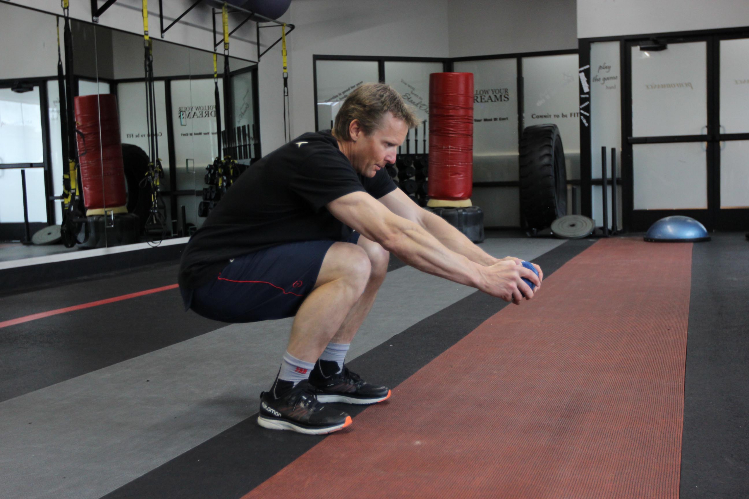 Man does a squat in gym while holding a medicine ball