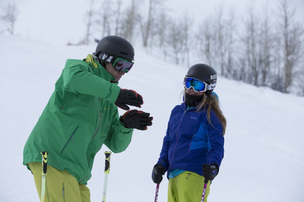 An alpine instructor uses their hands to demonstrate technique to their student
