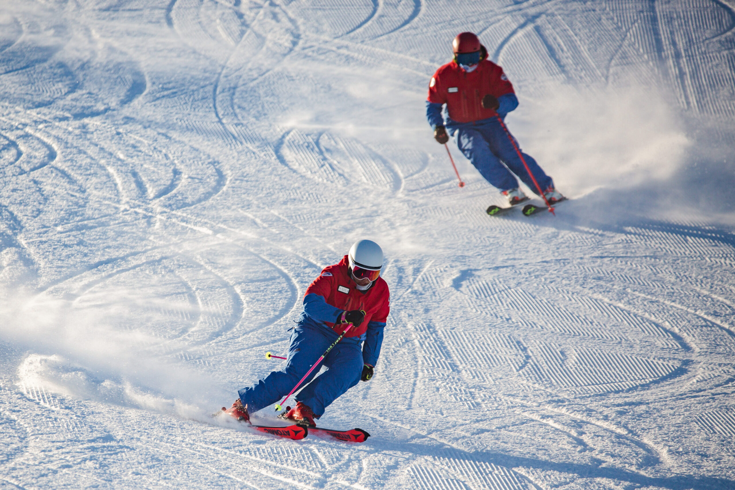 Two skiers carving a groomed run in sync.