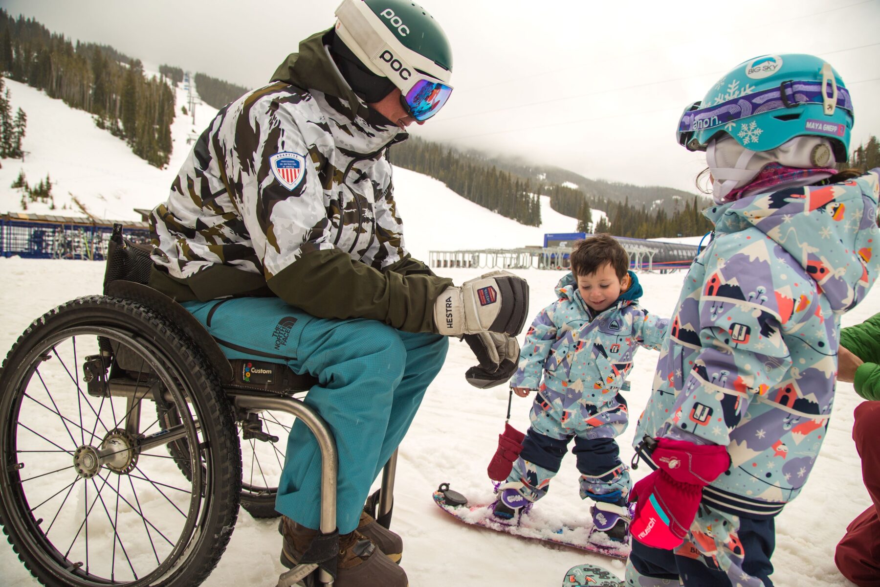 Skier in wheelchair with two kids on snowboards